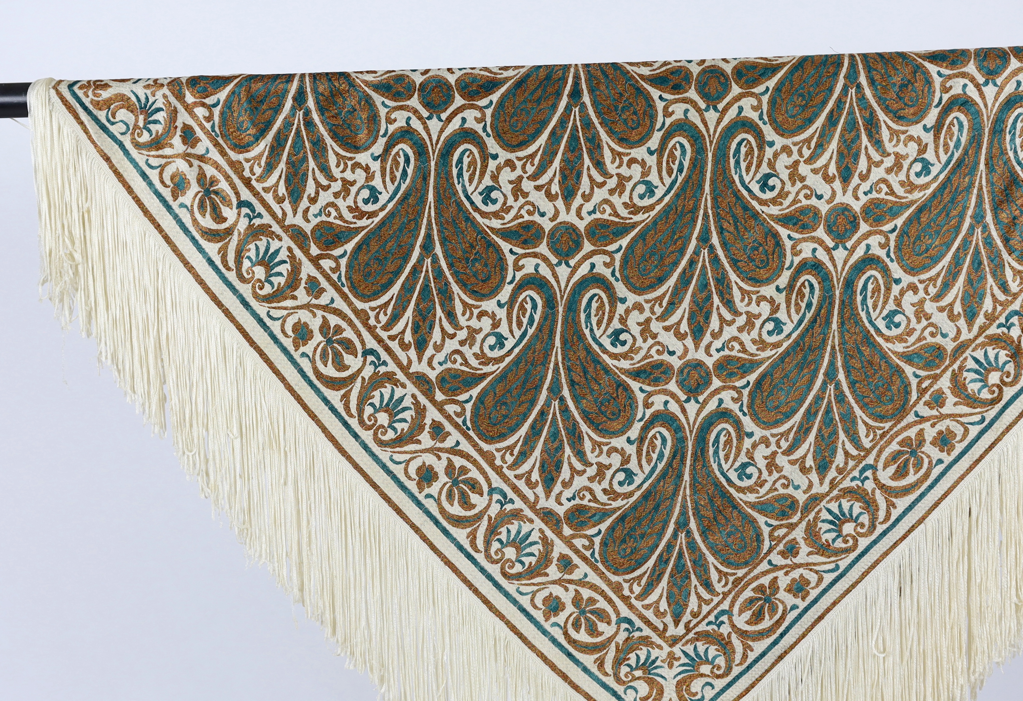 A 1920’s-1930’s cream silk woven shawl, woven with turquoise and bronze coloured silks in an all over tear drop paisley motif, edged with fine knitted cream fringing, approximately 109cm x 120cm